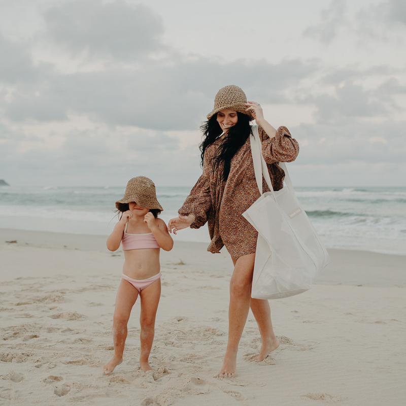A mother and daughter are walking at the beach. The mother is carrying a the Sande Kids Beach Hauler oversized beach bag tote.