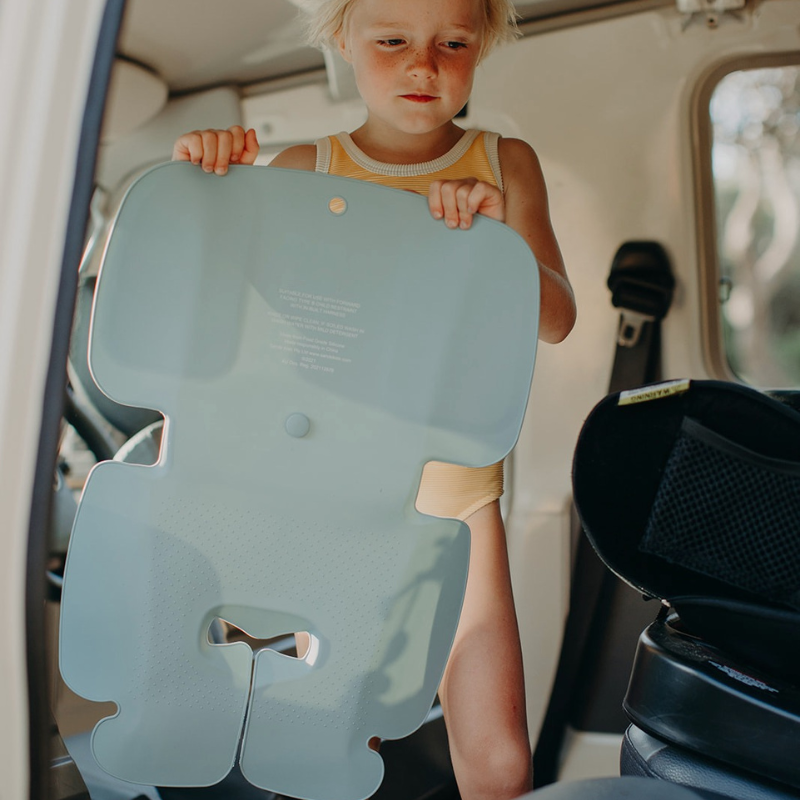 A little girl with blonde hair in a yellow swimming costume unrolling her Sande Kids™ Waterproof Car Seat liner to use in her car seat for the trip home from the beach.