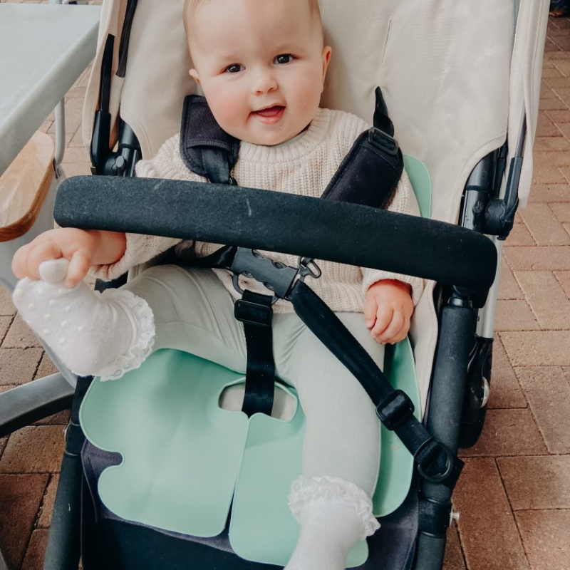 A baby girl sitting in her Bugaboo pram with a Seafoam Green Sande Kids™ silicone car seat and pram liner.