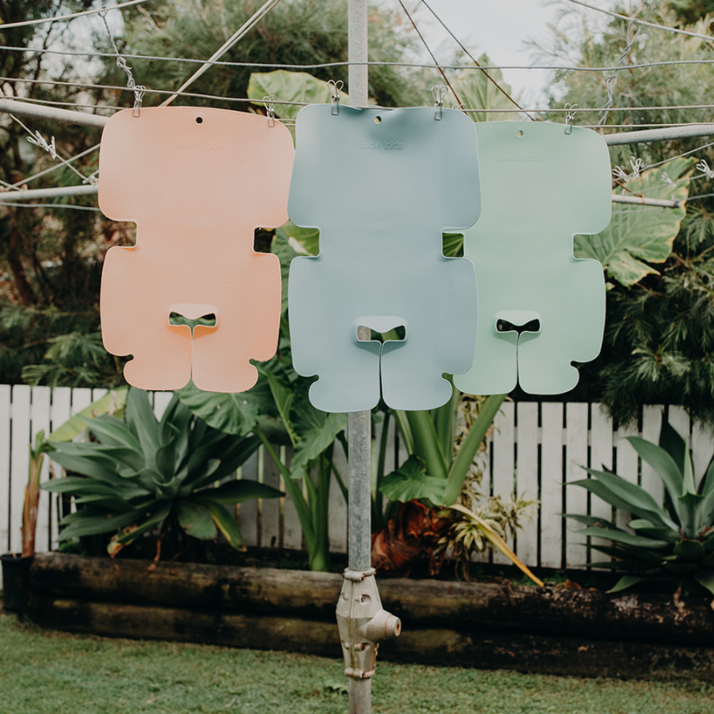 The colour options available for the silicone Sande Kids™ Waterproof Car Seat and Pram Liner  hanging on an old hills hoist clothes line in a back yard.